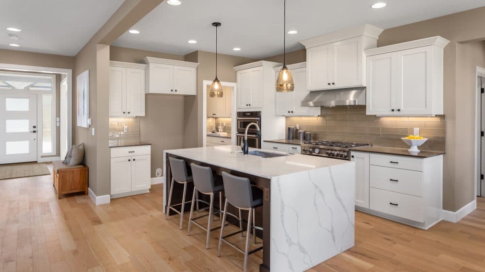 A modern white kitchen with stone countertops and recessed and pendant lighting