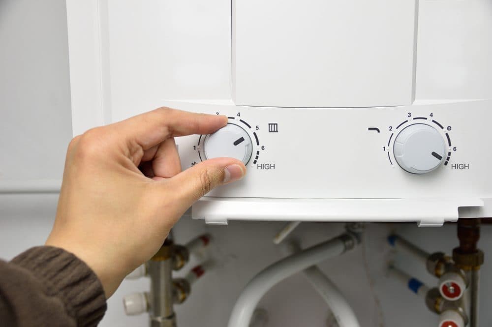 A hand adjusting the left knob on a tankless water heater