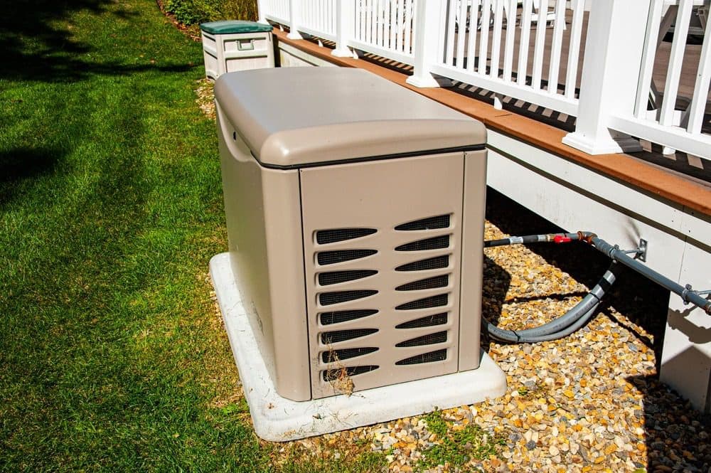 A generator sitting outside next to a back deck in a well manicured lawn