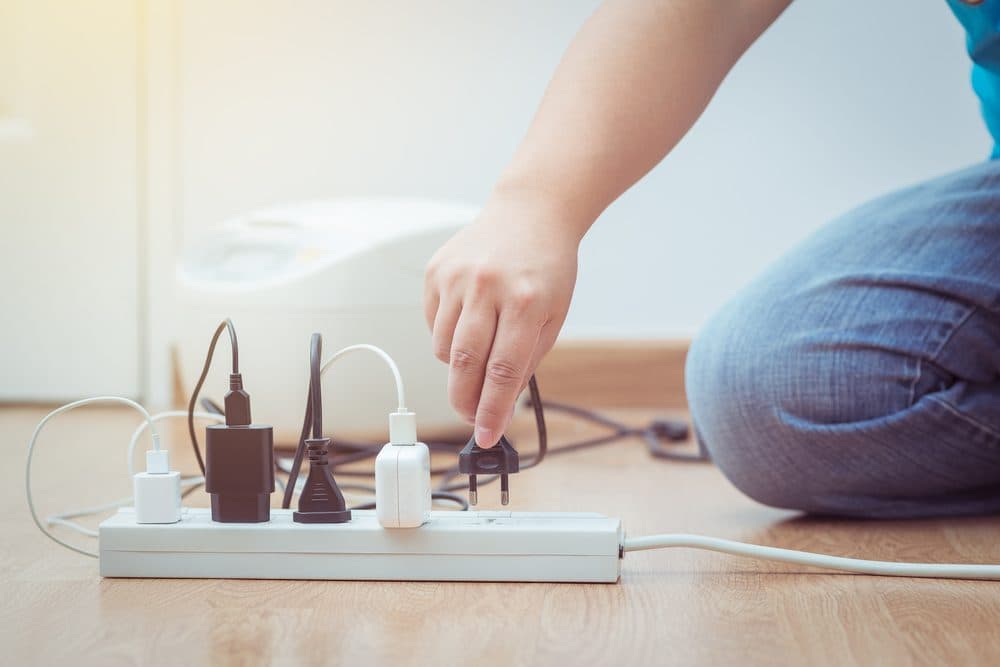 A woman plugging a plug into a surge protector that already has four plugs in it