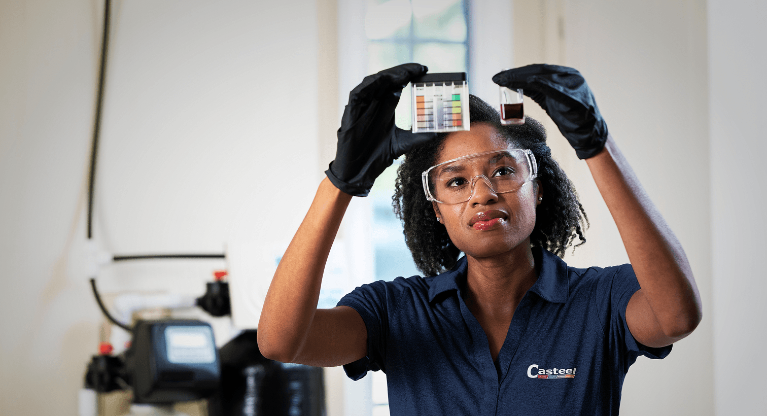 A professional Casteel technician conducting a home water quality test next to a residential water treatment filtration system.