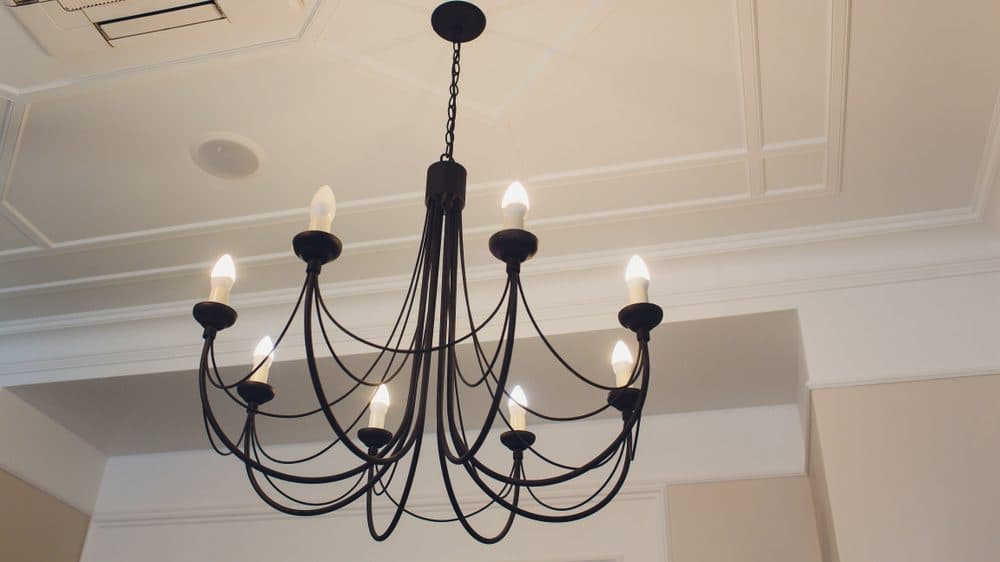 A black chandelier with draping details in a room with high ceilings and crown moulding