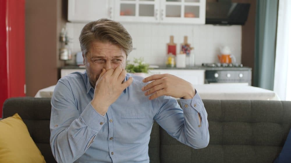 A homeowner in distress who is putting his index and thumb finger around his nose because of a stinky smell