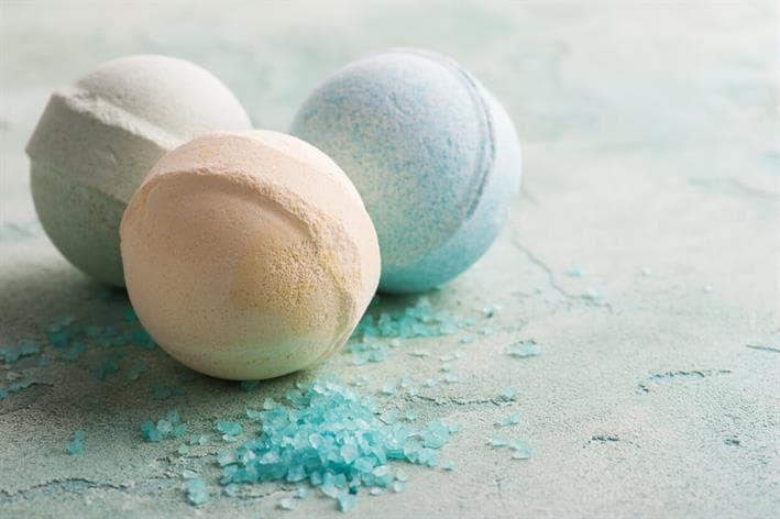 Orange, white, and blue bath bombs sitting next to small blue particles