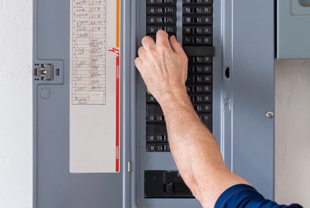 A technician reaching into a circuit panel to flip breakers