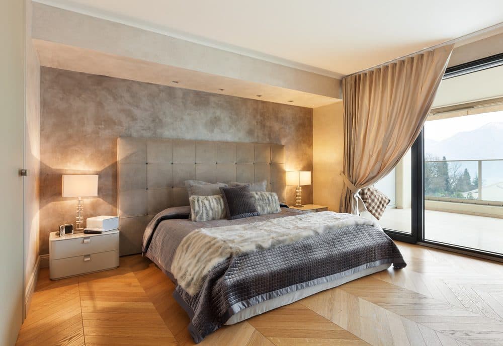 An upscale bedroom with beside lamps turned on, casting light upwards and downwawrds